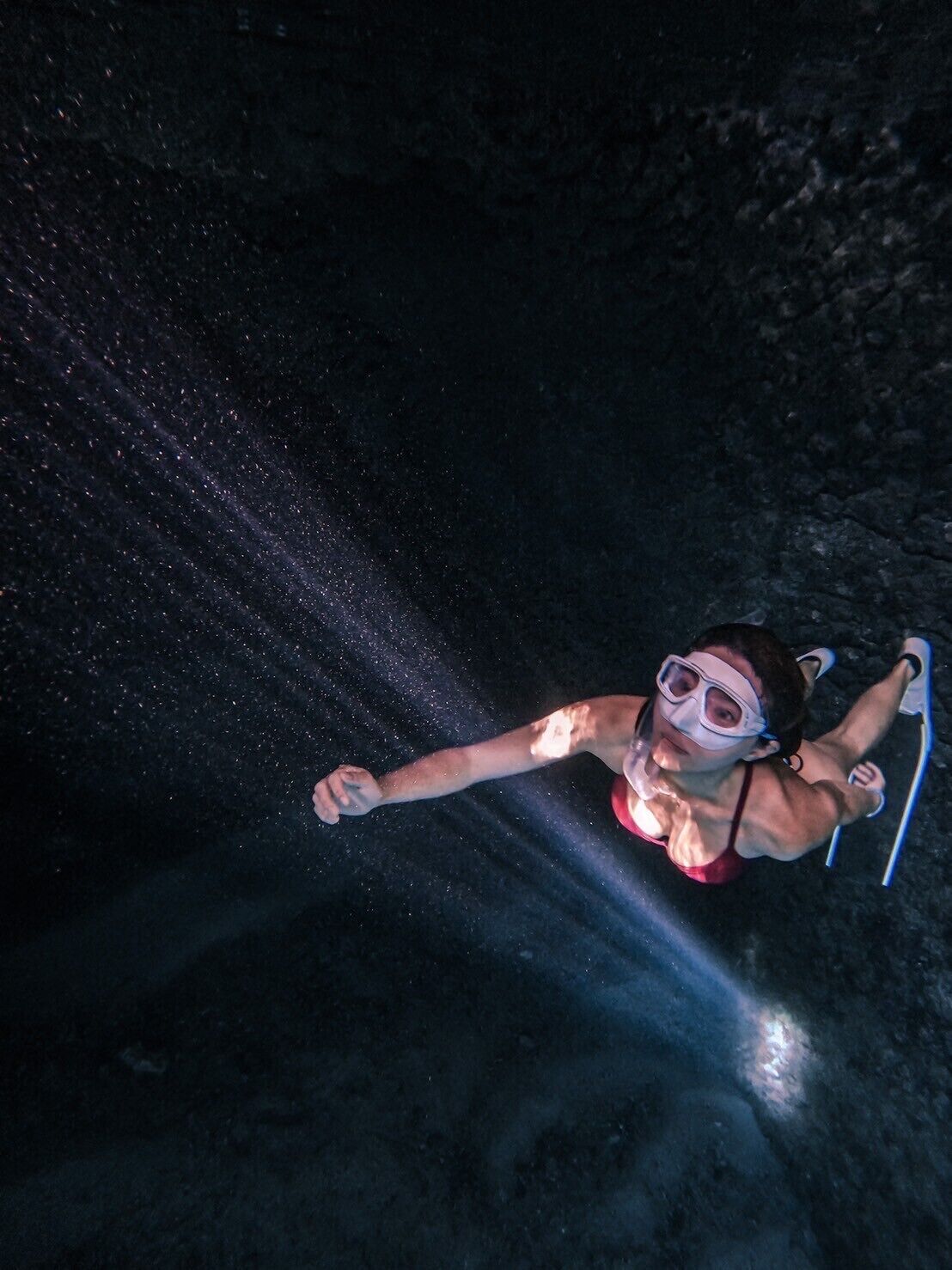 A person scuba diving in a dark underwater environment.
