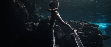 A person in a dark swimsuit standing on a rock with fins, underwater.