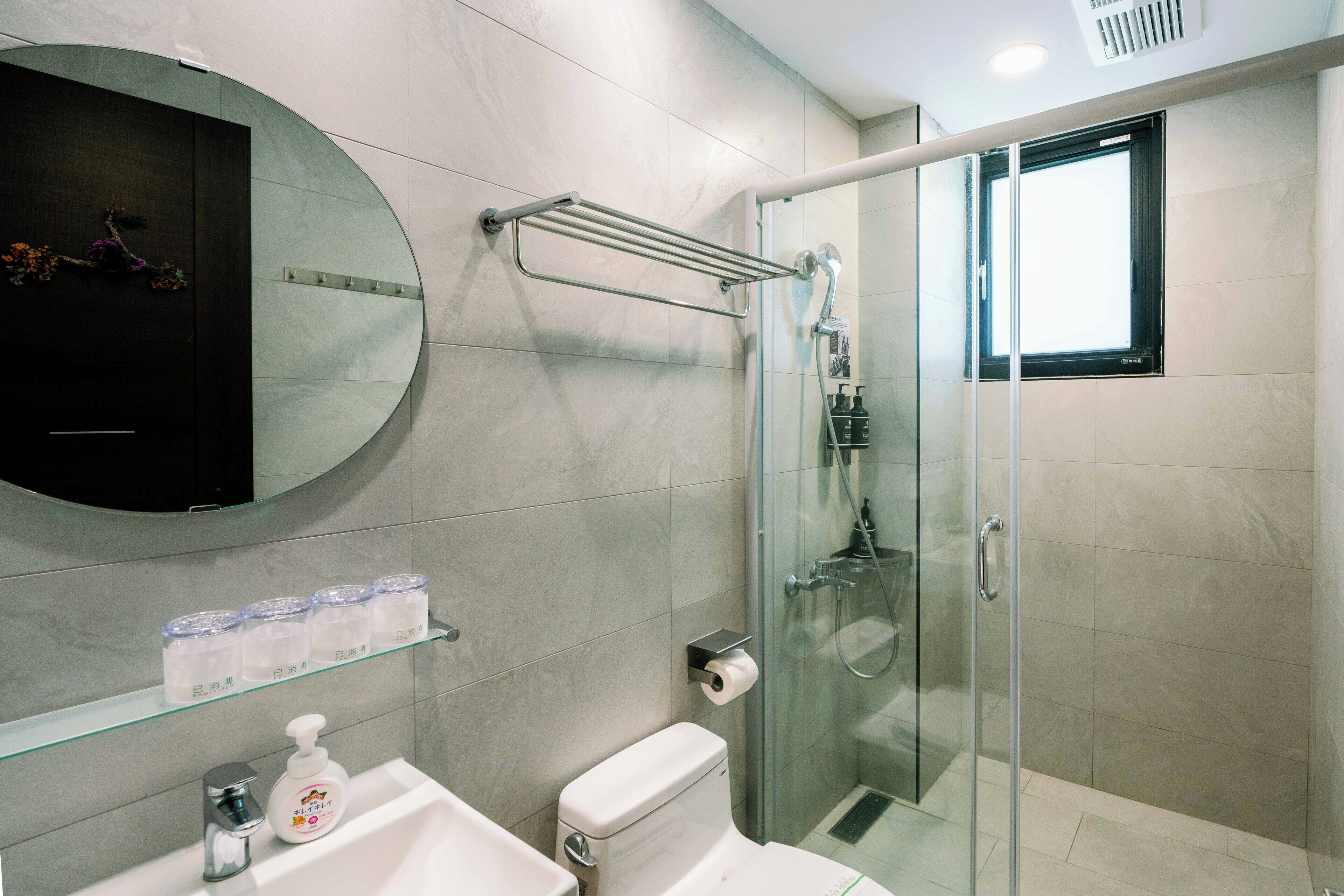 A modern bathroom with a glass shower enclosure, a toilet, a sink with a soap dispenser, and a mirror.