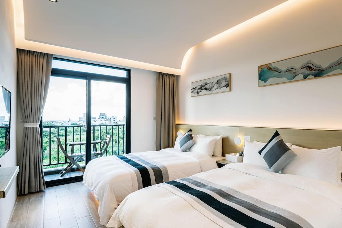 A hotel room with two beds, a balcony with a view, and artwork on the walls.