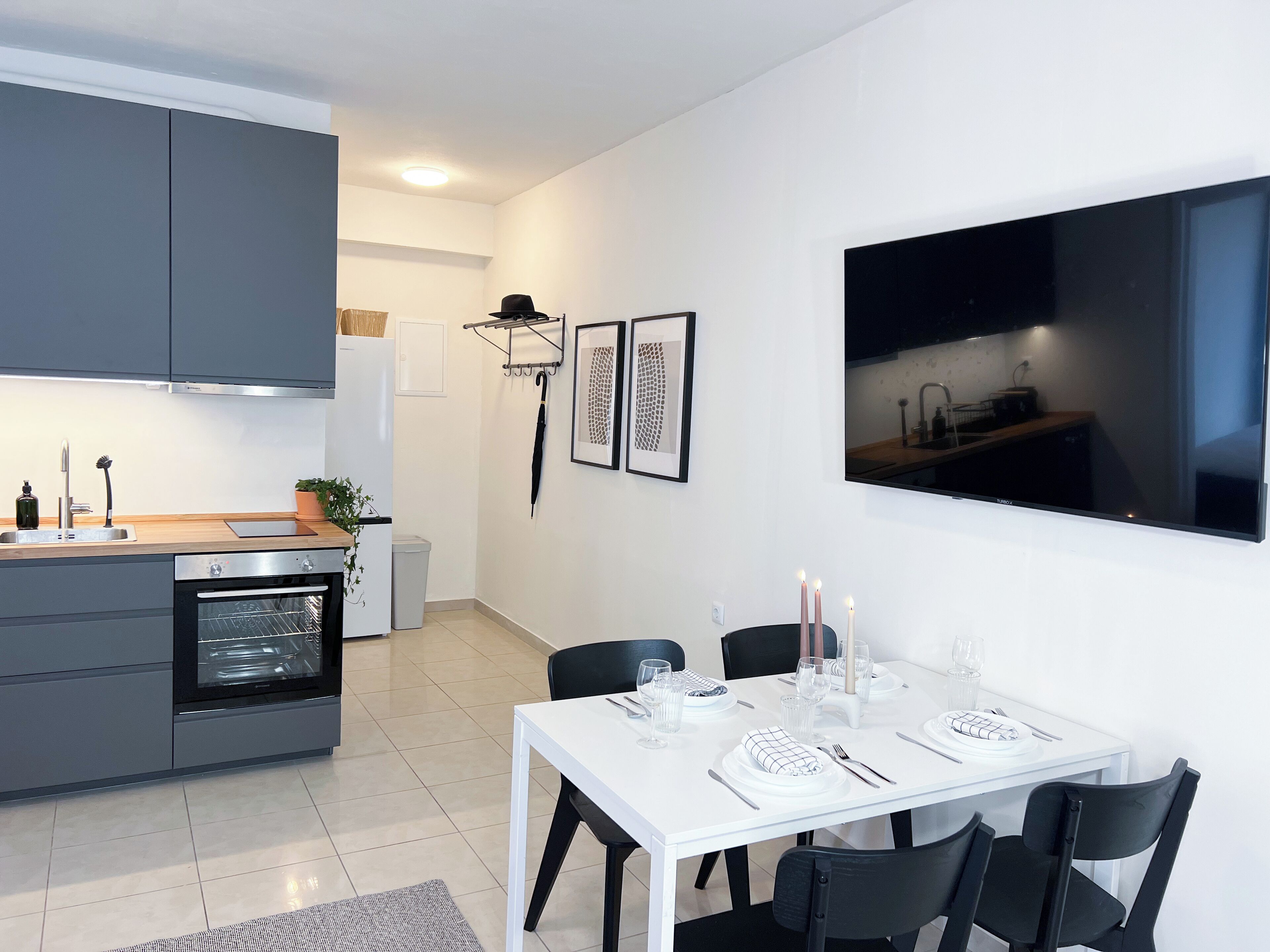 A modern kitchen with grey cabinets, a built-in oven, and a dining area with a white table set for four.