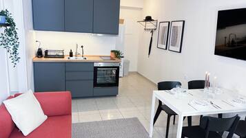 A modern kitchen with grey cabinets, a built-in oven, and a sink. There is a dining area with a white table and black chairs.