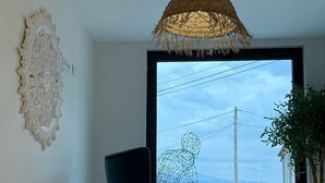 Egy modern szoba, nagy ablakkal, sötétzöld színű székkel, fonott mintájú mennyezeti lámpával és egy díszes falfelülettel.