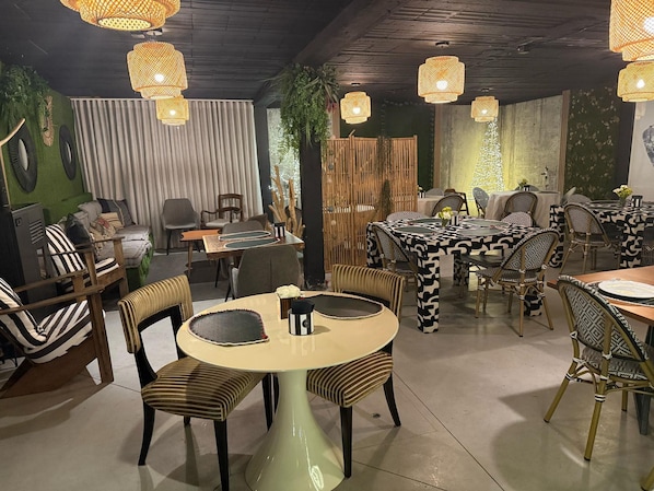 Un restaurant avec des tables et des chaises rondes, des lampes en osier suspendues et un mur végétal.