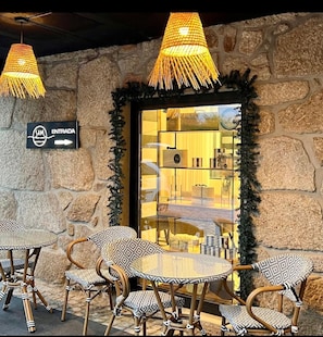 A stone wall entrance with a sign reading "ENTRADA" and a glass door leading inside. There are wicker tables and chairs outside. - Our Douro Design 3suites Jacuzzi Pool Flat (Cinfães)