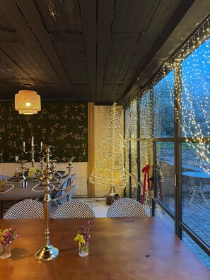 Un coin repas avec une table en bois, des chaises à motifs, un lustre et un sapin de Noël décoré de guirlandes lumineuses.