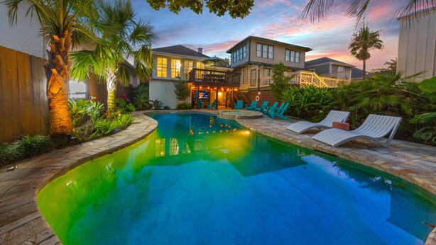 A swimming pool with lounge chairs, a wooden deck, and a house with a balcony.