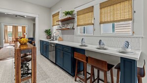A modern kitchen with dark blue cabinets, a white countertop, and a wooden bar stool area.