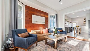 A spacious living room with a wooden accent wall, a large window, and a view into the kitchen.