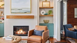 A living room with a fireplace, a large framed picture, and a blue armchair.