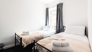 A bedroom with two single beds, a window with curtains, and a bedside table with a lamp. - Central House in Southampton (Freemantle)