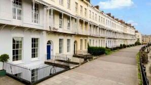A row of traditional terraced houses with uniform architecture, a paved street, and a clear sky.