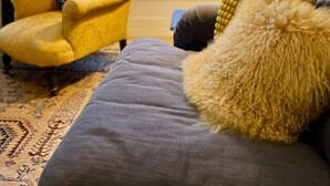 A cozy living room with a yellow armchair, a grey sofa with a fluffy yellow pillow, and a floor lamp.
