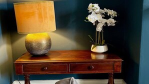 A wooden bedside table with a lamp and a vase of white flowers against a dark wall.