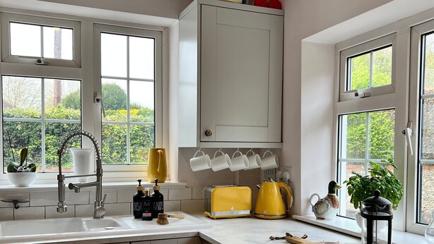 A kitchen with white cabinets, a sink, a toaster, a kettle, and a window with a view of greenery.
