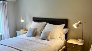 A bedroom with a large bed, two bedside tables with lamps, a wooden ceiling beam, and a carpeted floor.