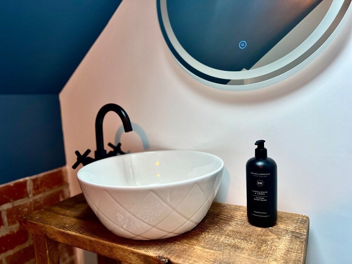 A white ceramic basin with a black faucet on a wooden countertop, next to a black bottle of hand soap.