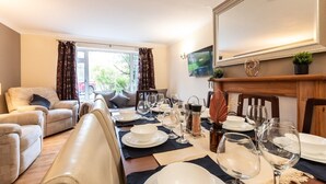 Un comedor con una mesa dispuesta para cuatro, un sofá y un televisor colgado en la pared.