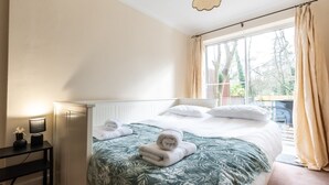 Un dormitorio con una cama, una mesita de noche con lámpara y una ventana con cortinas.