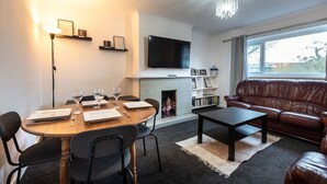 A modern living room with a fireplace, a flat-screen TV, a leather sofa, and a dining area with a round table and chairs. - Central Flat, Off-Road Parking (Shirley)