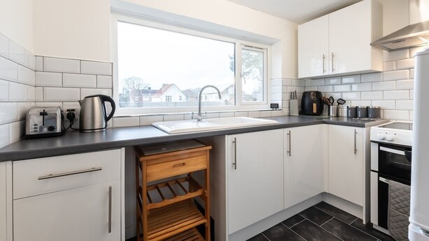 A modern kitchen with white cabinets, a black countertop, a window, and a built-in oven. - Central Flat, Off-Road Parking (Shirley)
