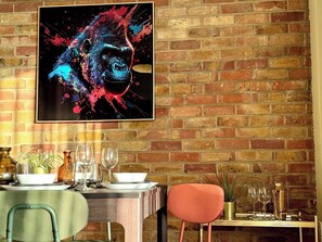 Un coin repas avec un mur en briques, une table dressée pour deux personnes et une œuvre d’art encadrée au-dessus de la table.