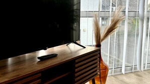 Un salon moderne avec un téléviseur à écran plat posé sur un meuble en bois, une télécommande et un vase contenant des plantes séchées.