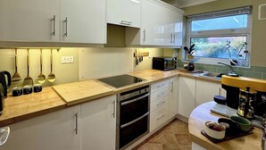 Une cuisine moderne avec des meubles blancs, un four encastré, un four à micro-ondes et une fenêtre donnant sur un espace verdoyant.
