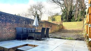 Un patio al aire libre con un muro de ladrillo, una mesa con sillas y una valla de madera.