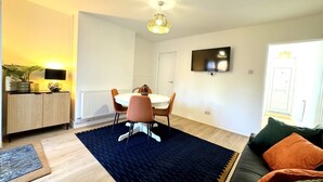 Una sala de estar moderna con comedor, un sofá, una mesa de centro y un televisor montado en la pared.