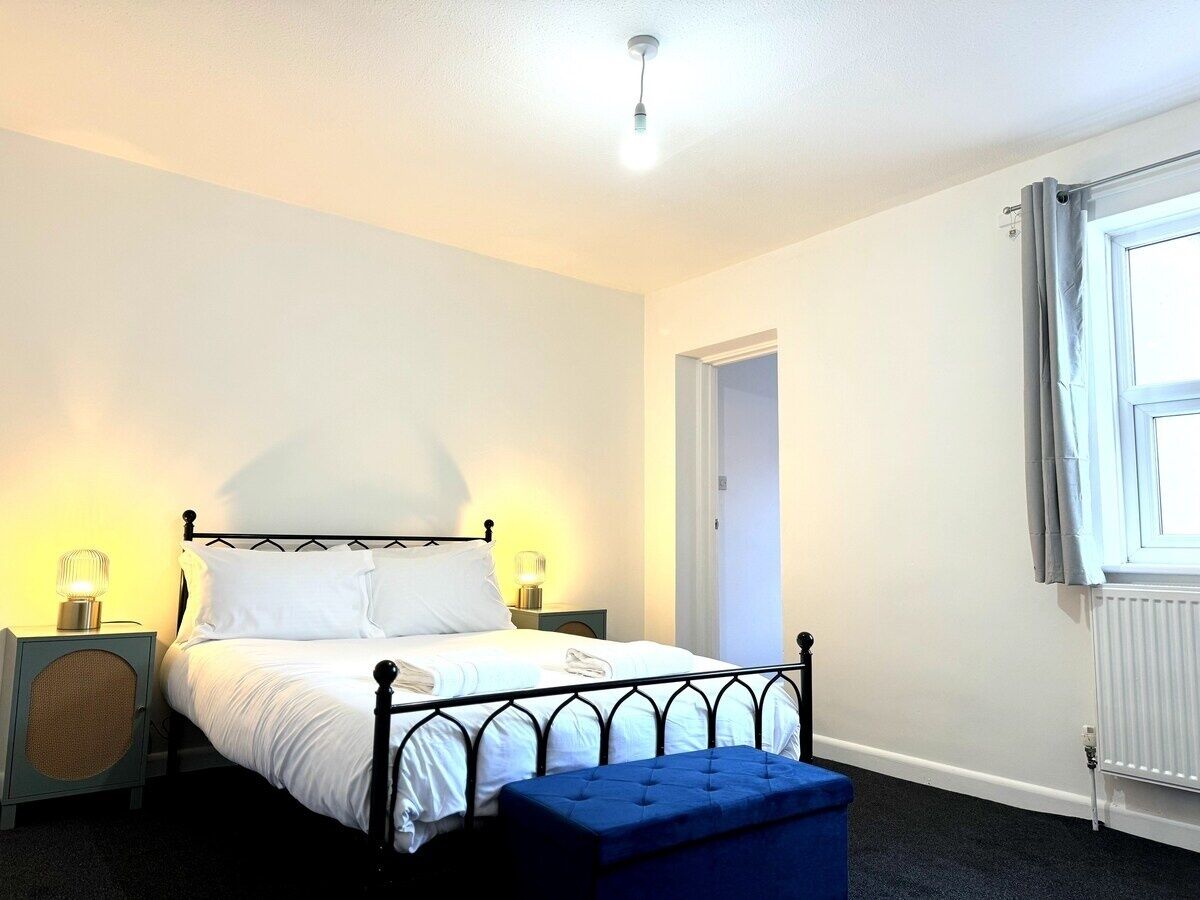 Ein Schlafzimmer mit Bett, Nachttischlampen, einer blauen Bank, einem Heizkörper und einem Fenster mit Vorhängen.