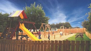 Une aire de jeux avec un toboggan, des balançoires et des tables de pique-nique.