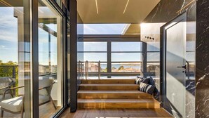 Interior moderno com escada de madeira que dá para uma varanda, janelas amplas e vista para a paisagem urbana.