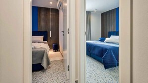 Quarto de hotel com cama, uma pequena mesa, uma cadeira e uma janela com cortinas.