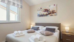Una habitación de hotel con cama, almohadas, una mesita de noche, una lámpara y un cuadro en la pared.