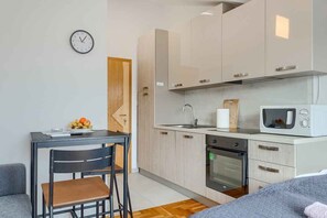 A compact kitchen with a microwave, oven, and sink. There's a dining area with a table and chairs. - Studio with air conditioning and balcony (Medulin)