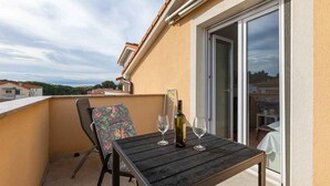 A balcony with a table, two chairs, a bottle of wine, and a glass.