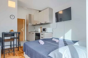 A modern hotel room with a bed, a desk with a chair, a microwave, and a TV mounted on the wall. - Studio with air conditioning and balcony (Medulin)