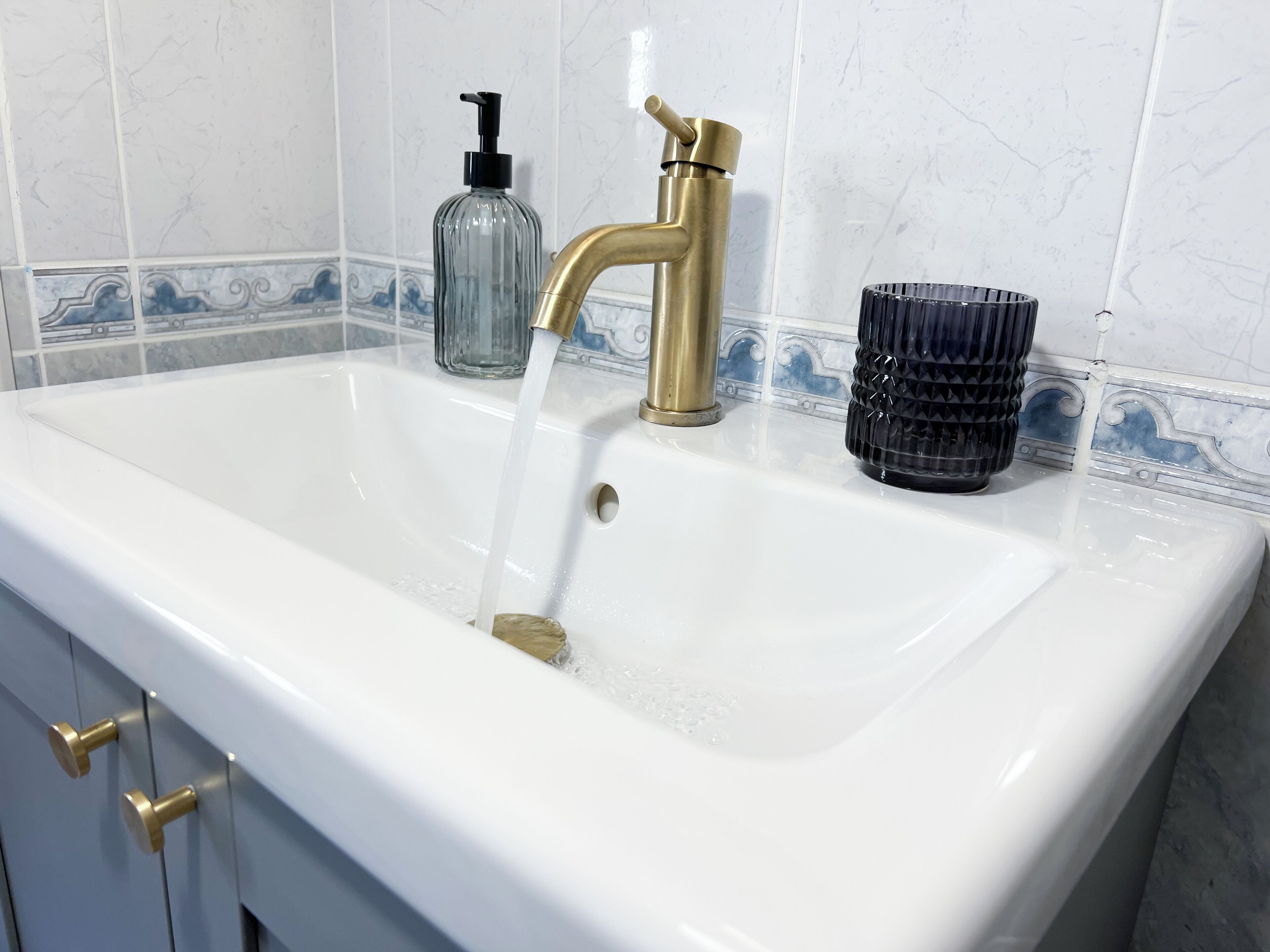 A bathroom sink with a gold faucet, a soap dispenser, and a glass container.
