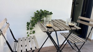 Une table en bois avec deux chaises, une plante en pot et deux verres de café sur un balcon.