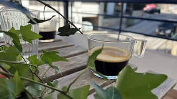 Una taza de café sobre una mesa de madera con hojas verdes al frente.