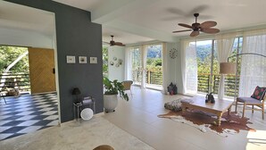 A spacious living area with a large window, ceiling fans, a wooden table, and a dog resting on a checkered floor. - Casa Li Tayrona (Santa Marta)
