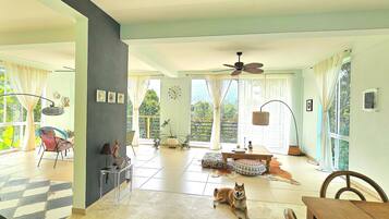 A spacious living area with a large window, a ceiling fan, and a dog lying on the floor.