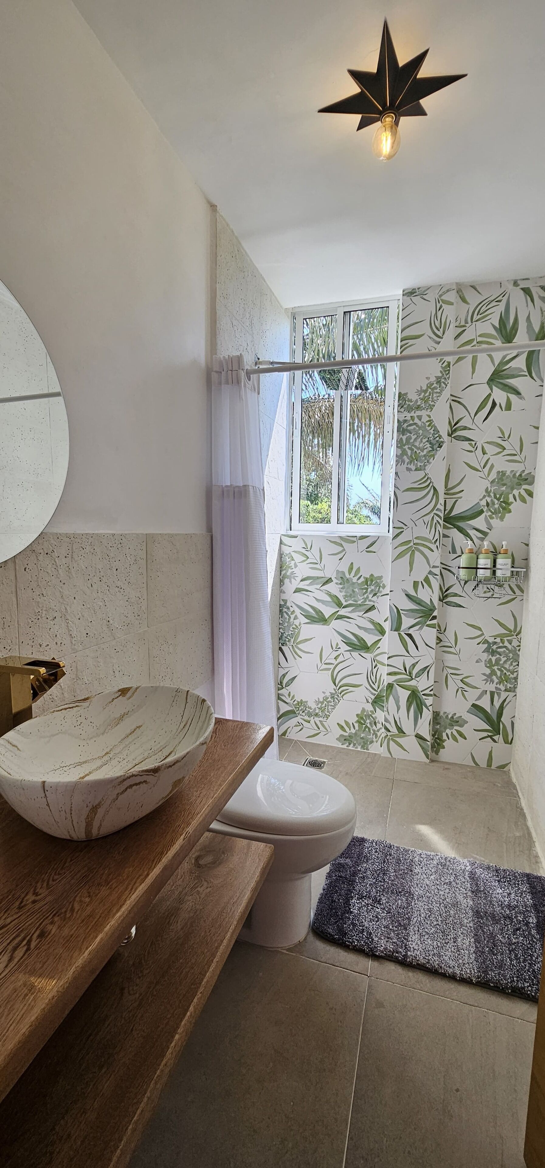 Un baño con tocador de madera, espejo redondo, lavabo blanco, inodoro y cortina de ducha.