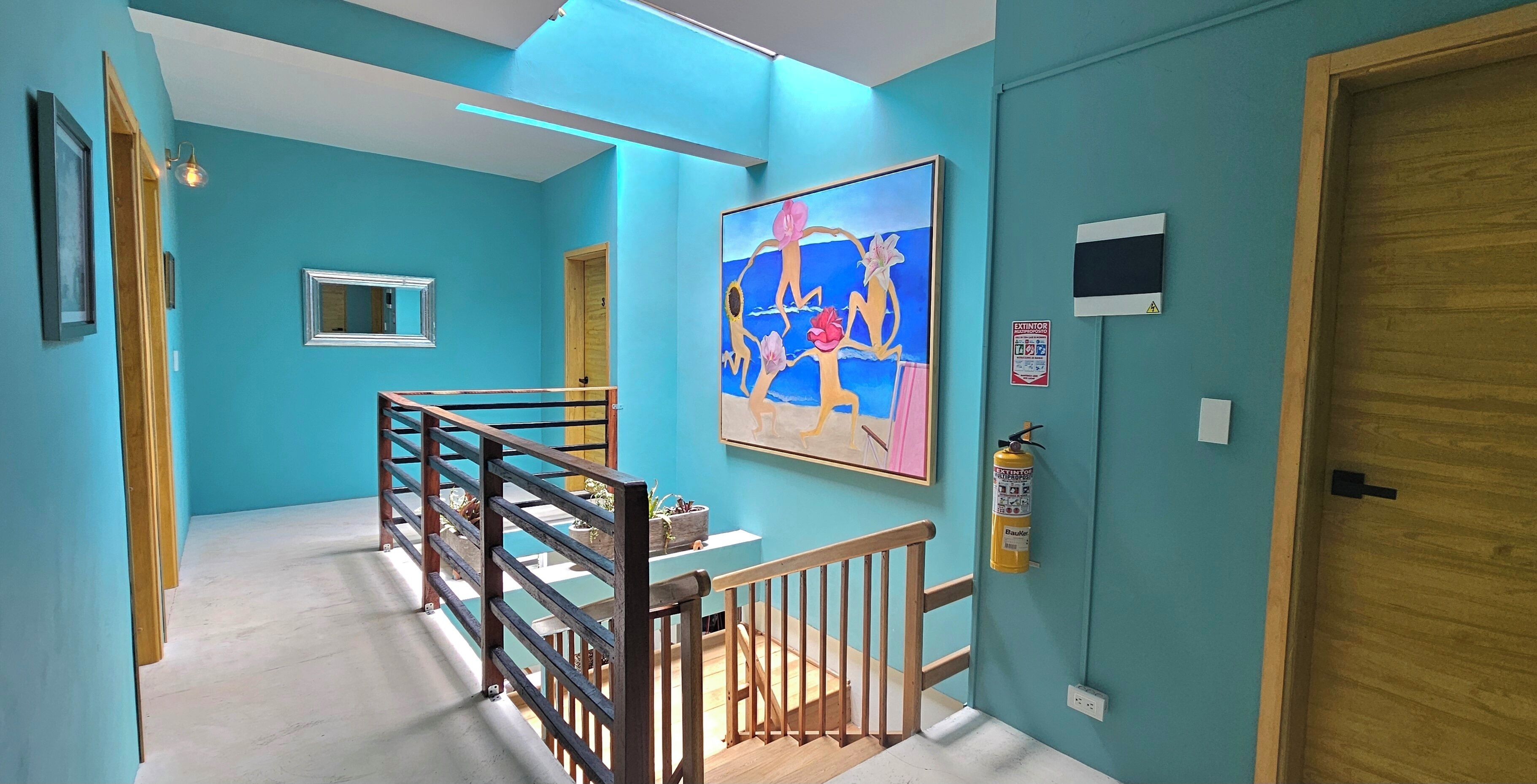 A hallway with teal walls, a wooden door, a fire extinguisher, and a framed abstract painting.