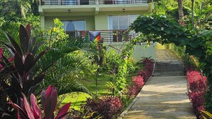 A multi-story building with balconies, surrounded by lush greenery and a concrete pathway leading to the entrance. - Casa Li Tayrona (Santa Marta)