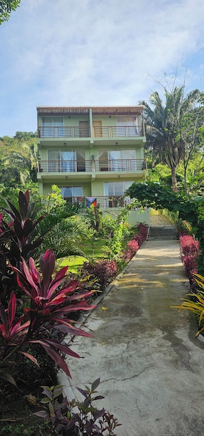 A multi-story building with balconies, surrounded by lush greenery and a concrete pathway leading to the entrance. - Casa Li Tayrona (Santa Marta)
