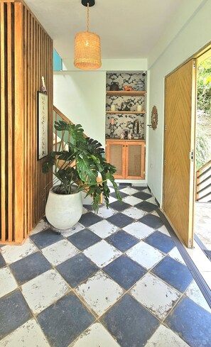 Un couloir avec un sol à carreaux, une plante en pot, un luminaire suspendu et une porte en bois.