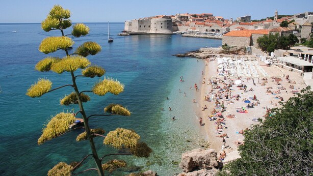 A coastal town with a beach, clear waters, and historic buildings.