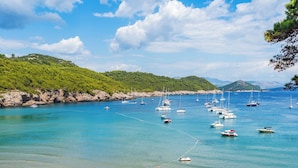 A coastal area with boats anchored in clear blue waters, surrounded by green hills.